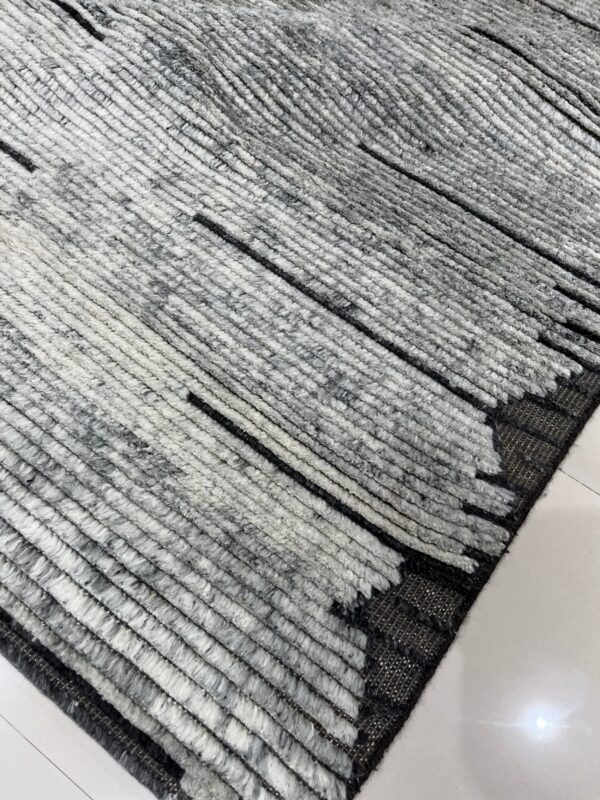 Close-up of a high-pile gray and white rug featuring thick textured ridges and thin black accent lines on white tile.