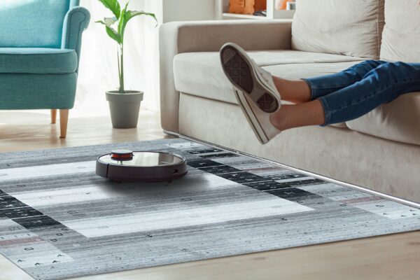 Gray geometric striped rug on wood flooring with a robot vacuum, sofa, and teal armchair.