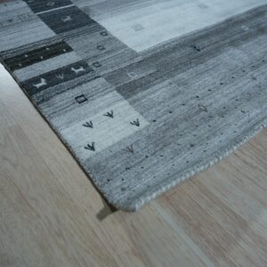 Light gray and dark gray striped rug with geometric and tribal patterns on blonde wood floor.