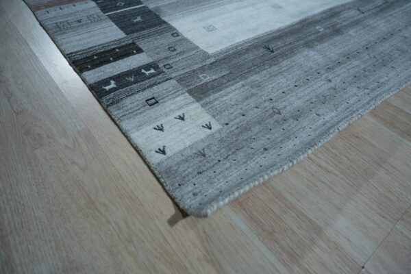 Light gray and dark gray striped rug with geometric and tribal patterns on blonde wood floor.