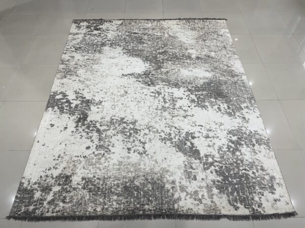 Abstract gray and white rug with short pile and dark fringe rests on a reflective tile floor.