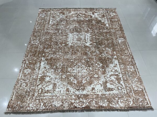 Low-pile rug with a faded brown and cream ornate pattern displayed on a reflective tiled floor.