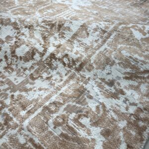 Close-up of a beige and white rug featuring a distressed abstract pattern and varied pile height texture.