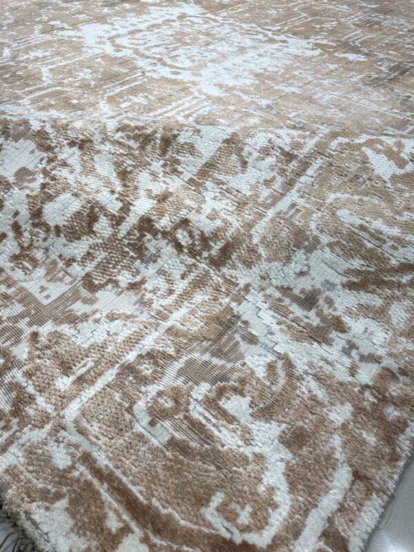 Close-up of a beige and white rug featuring a distressed abstract pattern and varied pile height texture.