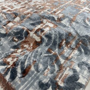 Textured high-low rug in gray, white, and brown with abstract motifs and matching colored fringe visible on the floor.