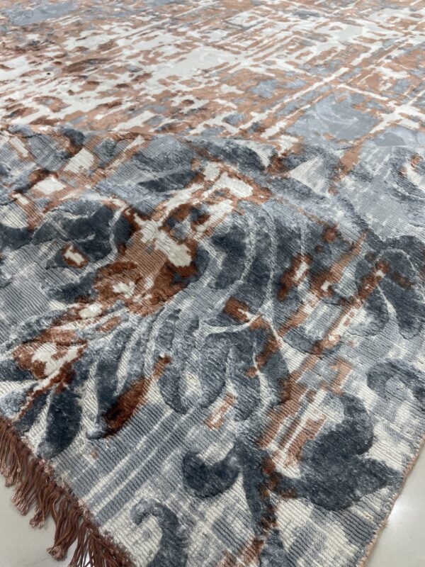 Textured high-low rug in gray, white, and brown with abstract motifs and matching colored fringe visible on the floor.