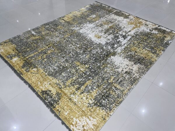Distressed abstract rug in gold, gray, and white resting on a reflective, light gray tile floor.