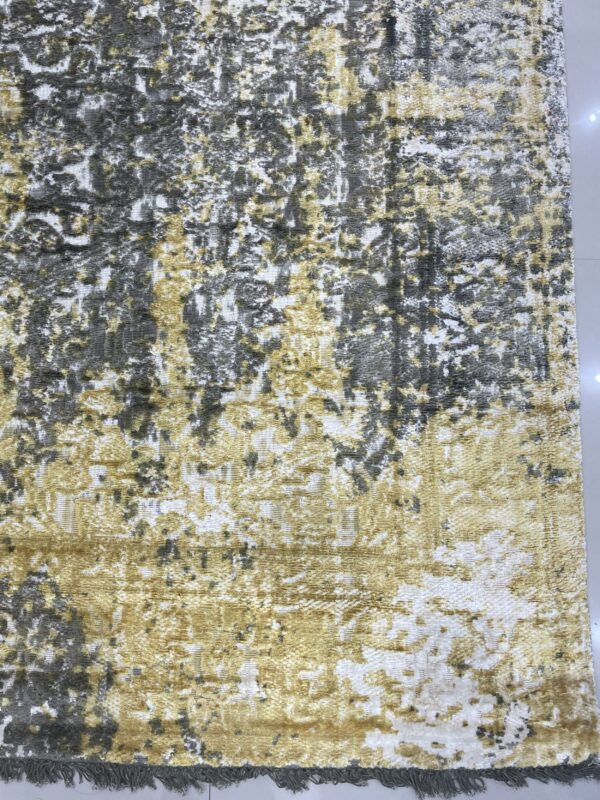Textured abstract rug in white, gray, and gold tones on a reflective tile floor with visible fringe.