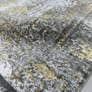 A folded rug featuring a mottled gray, white, and yellow textured pattern with visible fringe.