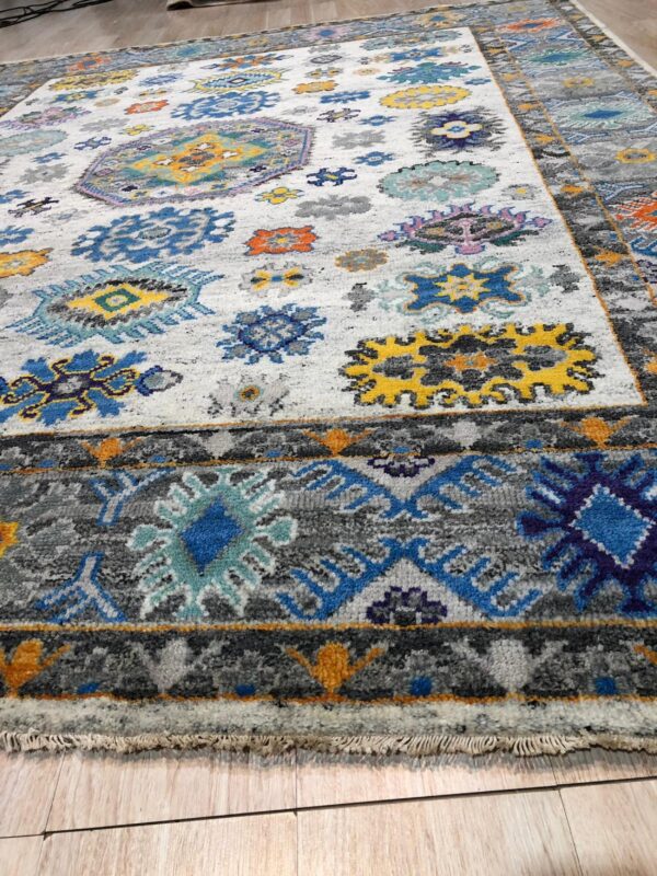 Low-pile rug in white, gray, blue, and yellow with abstract medallions on light wood flooring.