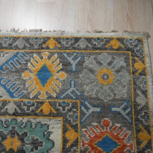 Close-up of a gray rug featuring geometric patterns in yellow, blue, teal, and pink on wood flooring.