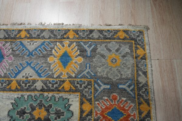 Close-up of a gray rug featuring geometric patterns in yellow, blue, teal, and pink on wood flooring.