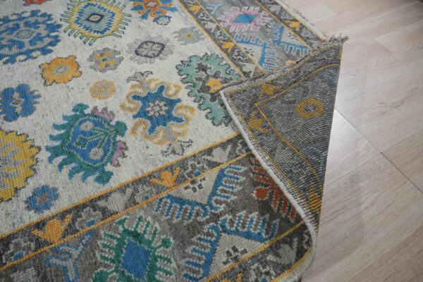 Multicolor rug with blue, yellow, and gray floral patterns, flipped to show the dense woven backing on pale wood floors.