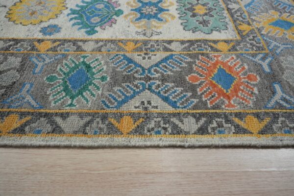 Light gray and dark gray rug with bright blue, orange, and yellow geometric motifs on light wood floor.