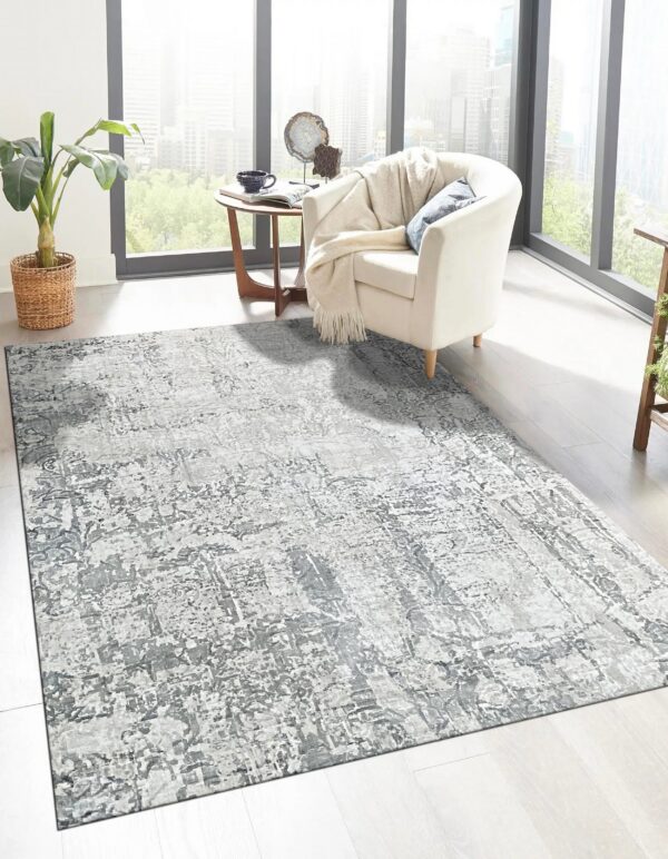 Gray abstract rug defines a sunny living space with light flooring and a white armchair near large windows.
