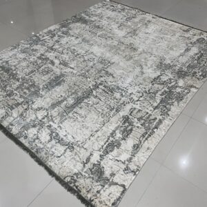 Distressed gray and cream area rug with fringe is displayed on a shiny gray tiled floor.