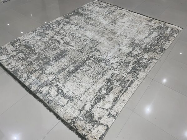 Distressed gray and cream area rug with fringe is displayed on a shiny gray tiled floor.