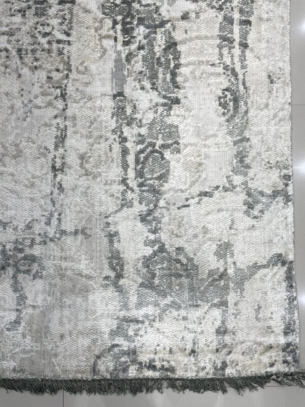 Textured white and gray abstract rug with dark fringe rests on a light tile floor.