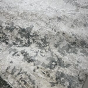 Textured grey and white rug featuring a distressed abstract pattern and visible fringe edge on a light floor.