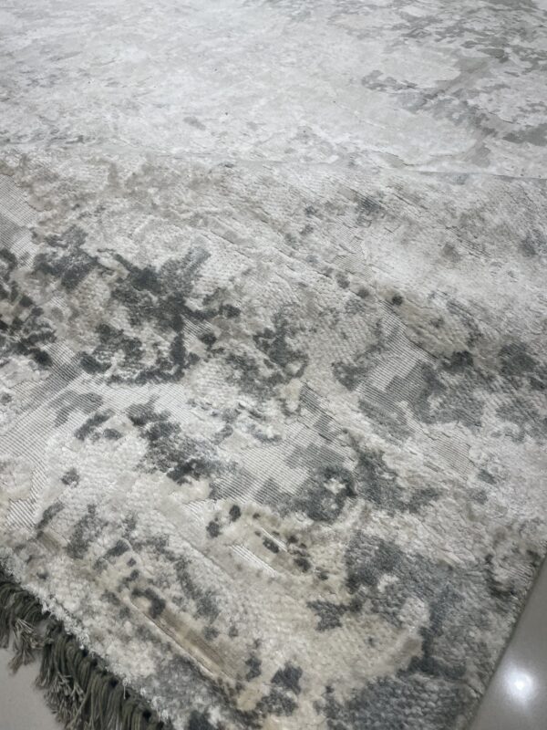 Textured grey and white rug featuring a distressed abstract pattern and visible fringe edge on a light floor.