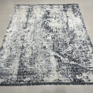 Abstract charcoal and white distressed area rug with short fringe rests on light gray tiled flooring.