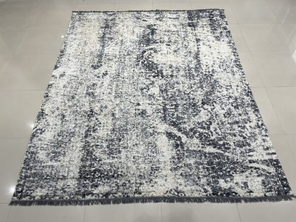 Abstract charcoal and white distressed area rug with short fringe rests on light gray tiled flooring.
