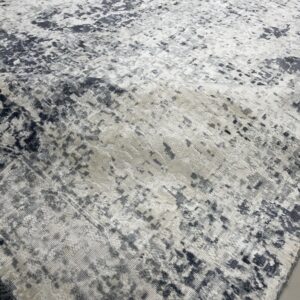 Abstract gray and white distressed rug with high-low texture lies on a light floor, showing dark fringe.
