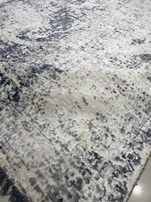 Abstract gray and white distressed rug with high-low texture lies on a light floor, showing dark fringe.