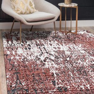 Rust, white, and black distressed rug on wood flooring beneath a gray chair and marble side table.