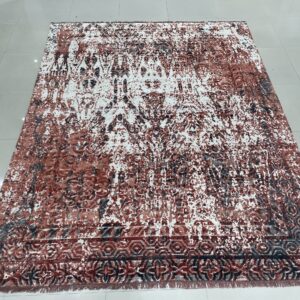 Rust and white distressed rug with geometric border lying flat on reflective gray tile flooring.