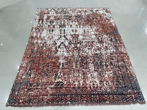 Rust and white distressed rug with geometric border lying flat on reflective gray tile flooring.