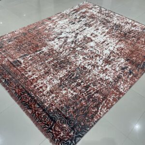 Rust, gray, and white abstract rug with a patterned border lying on shiny gray tile flooring.