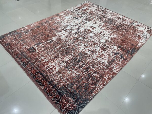 Rust, gray, and white abstract rug with a patterned border lying on shiny gray tile flooring.