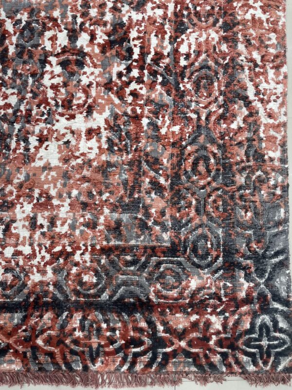 Close up of a ribbed pile rug in rust, charcoal, gray, and white abstract and ornate patterns.