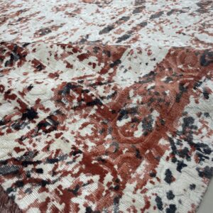 Textured rug detail showing mottled red, cream, and charcoal patterns with varying pile height and visible fringe.