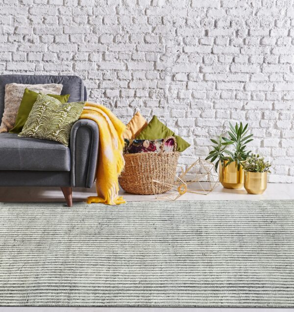 Textured gray and white striped rug with a gray sofa, woven basket, and gold planters nearby.