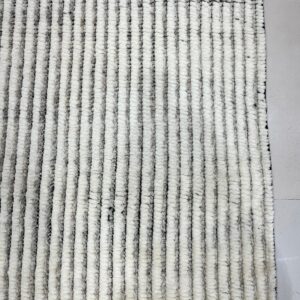 Thick, striped white and gray textured rug lying on a light gray square tiled floor.