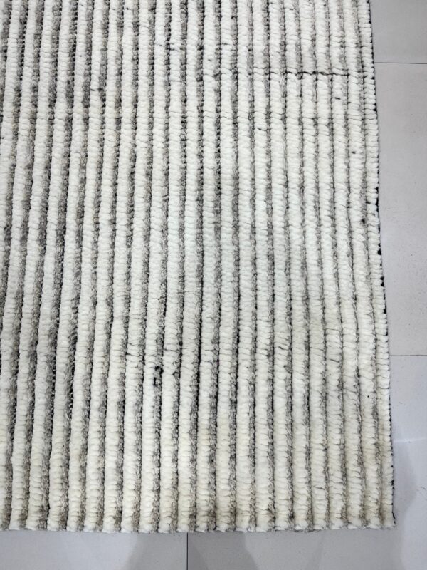 Thick, striped white and gray textured rug lying on a light gray square tiled floor.