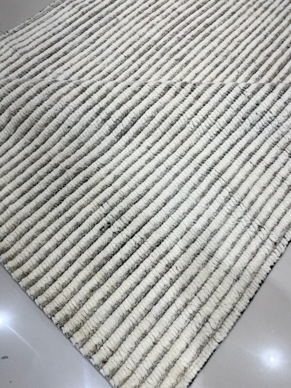 High-pile rug with alternating cream and gray thick ribbed stripes on a shiny white tile floor.