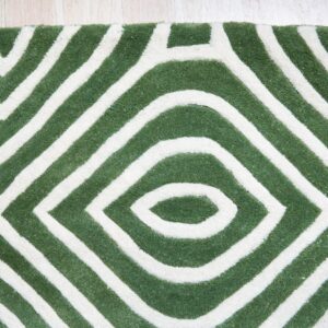 Textured green and white rug featuring thick, geometric stripes forming nested diamond shapes on wood flooring.
