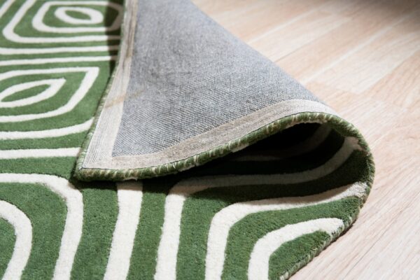 Geometric green and white rug is rolled back revealing its woven backing on light plank flooring.