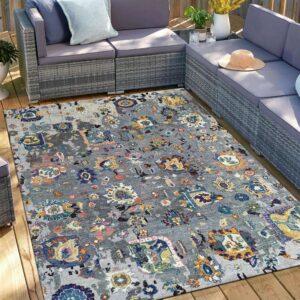 A gray abstract patterned rug sits under gray wicker furniture on a sunny wooden deck.