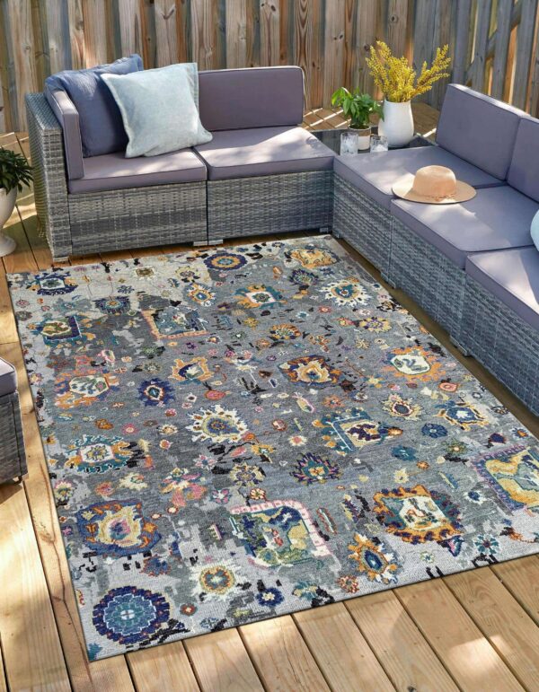 A gray abstract patterned rug sits under gray wicker furniture on a sunny wooden deck.