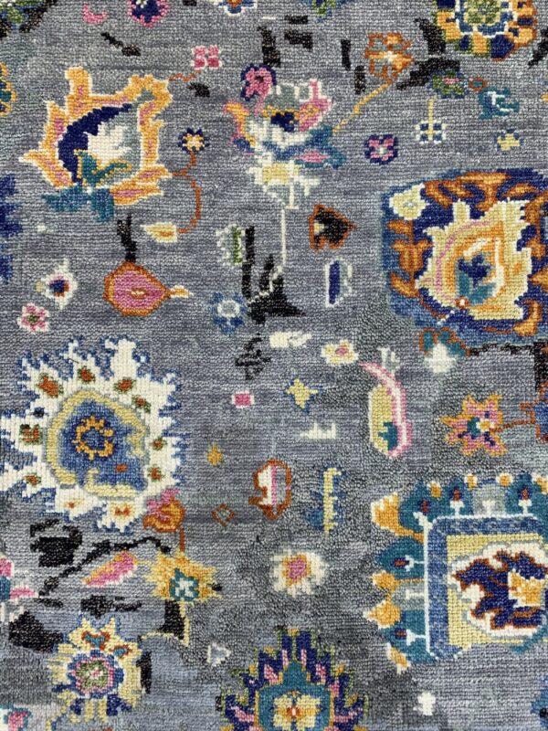 Close-up of a textured gray rug with scattered colorful stylized traditional patterns.