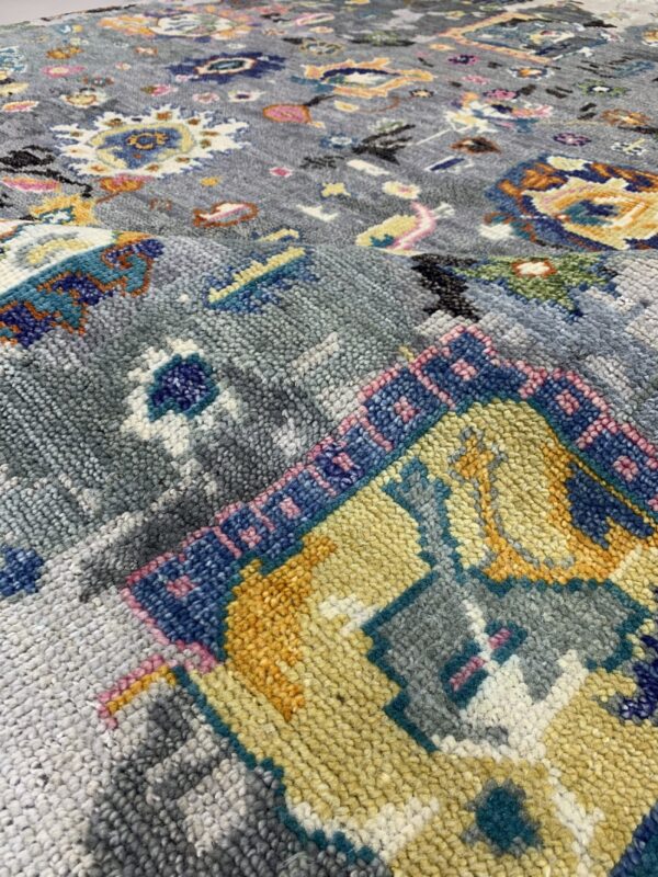 Detailed view of a grey high-pile rug with scattered blue, yellow, orange, and pink colorful patterns.