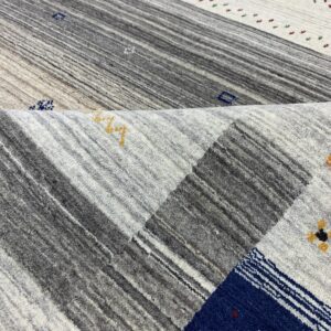 Close-up of a folded, textured rug featuring gray, white, and navy striped panels with tiny colorful accents.