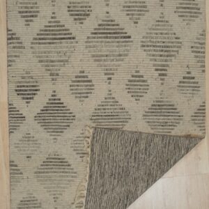 A low-pile rug with beige and dark gray geometric diamond patterns lies on a light wood floor, corner folded back.