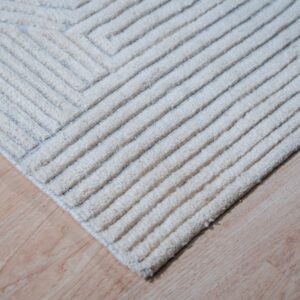 Close-up of a textured cream rug featuring raised geometric stripes and cord-like pile on light wood flooring.