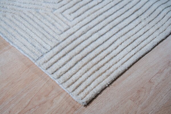 Close-up of a textured cream rug featuring raised geometric stripes and cord-like pile on light wood flooring.