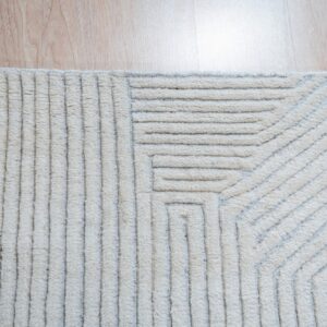 Textured cream rug featuring raised, parallel geometric stripes separated by recessed gray lines on wood flooring.